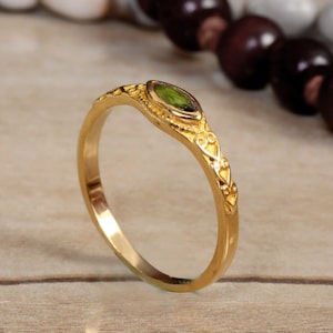 Può includere: Un anello d'oro con una pietra preziosa verde incastonata a forma di marquise. L'anello ha un design delicato e ornato.
