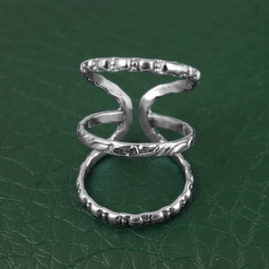 May include: Silver ring with three bands, each with a different textured design. The top band has a row of small beads, the middle band has a wavy design, and the bottom band has a row of small beads.