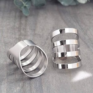 May include: Two silver rings with multiple bands. The rings are stacked on top of each other. The rings are made of metal and have a shiny finish.