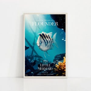 Puede incluir: Un p&oacute;ster enmarcado de la pel&iacute;cula "La Sirenita" de Disney, con el personaje Flounder. El p&oacute;ster tiene un fondo turquesa con elementos submarinos y el texto "Flounder" y "26 de mayo".