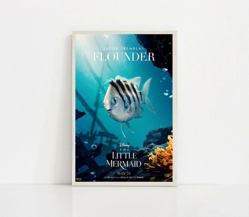 Puede incluir: Un p&oacute;ster enmarcado de la pel&iacute;cula "La Sirenita" de Disney, con el personaje Flounder. El p&oacute;ster tiene un fondo turquesa con elementos submarinos y el texto "Flounder" y "26 de mayo".
