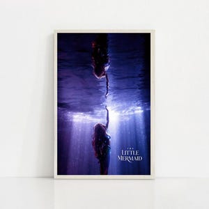 Puede incluir: Una impresi&oacute;n enmarcada con una escena de "La Sirenita". La imagen muestra a dos sirenas bajo el agua, una extendiendo la mano hacia la otra. La escena est&aacute; en tonos azules y morados, con rayos de luz. El t&iacute;tulo "THE LITTLE MERMAID" es visible.