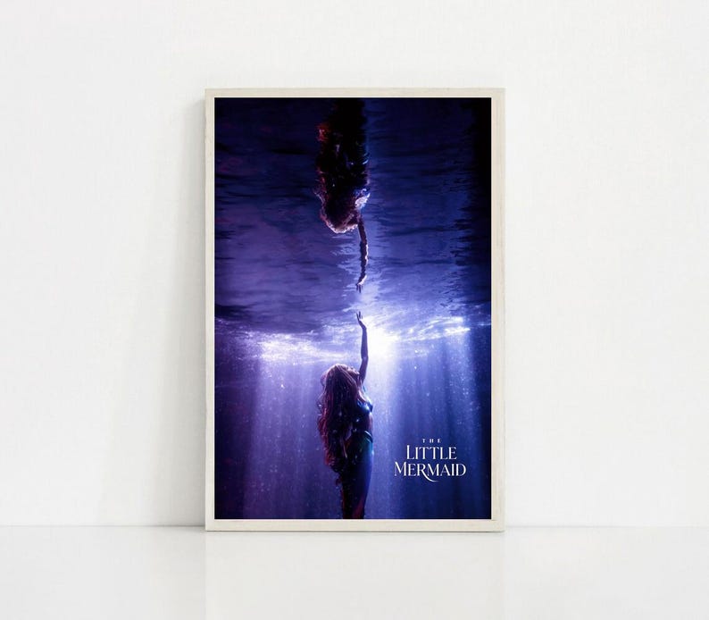 Puede incluir: Una impresi&oacute;n enmarcada con una escena de "La Sirenita". La imagen muestra a dos sirenas bajo el agua, una extendiendo la mano hacia la otra. La escena est&aacute; en tonos azules y morados, con rayos de luz. El t&iacute;tulo "THE LITTLE MERMAID" es visible.