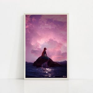 Puede incluir: P&oacute;ster enmarcado de una sirena sentada en una roca en el mar, con un cielo rosa y p&uacute;rpura de fondo. El p&oacute;ster incluye el texto "The Little Mermaid" en la parte superior.