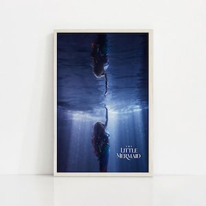 Puede incluir: Una impresi&oacute;n enmarcada que presenta una escena de "La Sirenita". La imagen muestra a dos sirenas, una extendiendo la mano hacia la otra bajo el agua. La escena est&aacute; ambientada en un oc&eacute;ano azul profundo con rayos de luz.