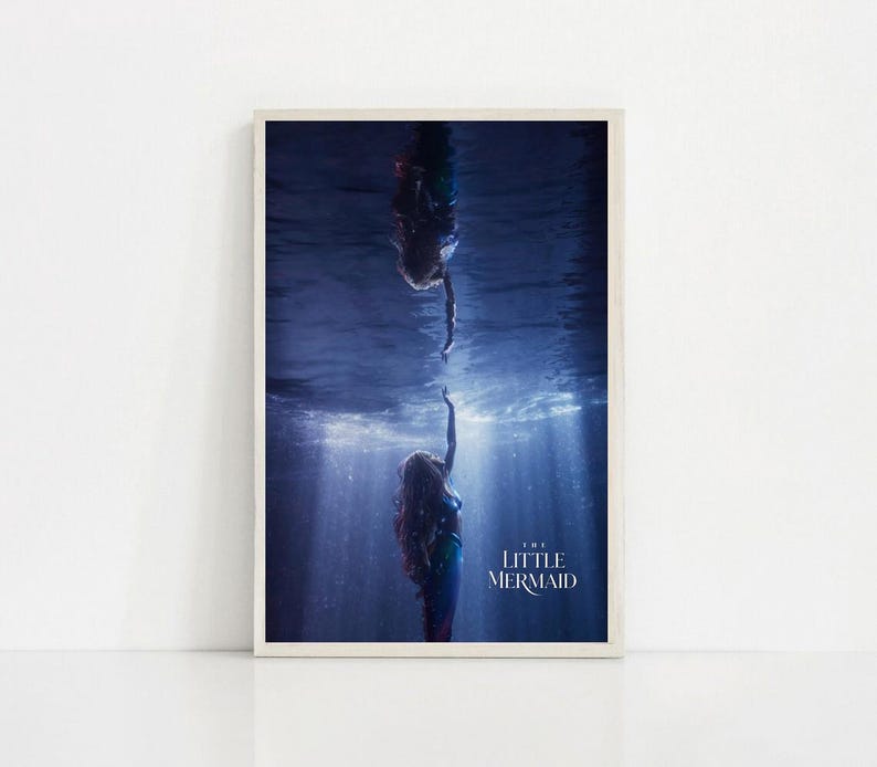 Puede incluir: Una impresi&oacute;n enmarcada que presenta una escena de "La Sirenita". La imagen muestra a dos sirenas, una extendiendo la mano hacia la otra bajo el agua. La escena est&aacute; ambientada en un oc&eacute;ano azul profundo con rayos de luz.