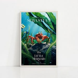Puede incluir: Un p&oacute;ster enmarcado de la pel&iacute;cula "La Sirenita" de Disney. El p&oacute;ster presenta una escena submarina con un cangrejo rojo, Sebasti&aacute;n, y el texto "La Sirenita" y "May 26". Algas verdes y un fondo azul completan el dise&ntilde;o.