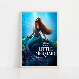 Puede incluir: Un p&oacute;ster enmarcado de "La Sirenita" de Disney. La imagen muestra a una sirena con largo cabello casta&ntilde;o rojizo y una cola turquesa, sentada en una roca. El fondo representa una escena submarina con luz solar y peces.