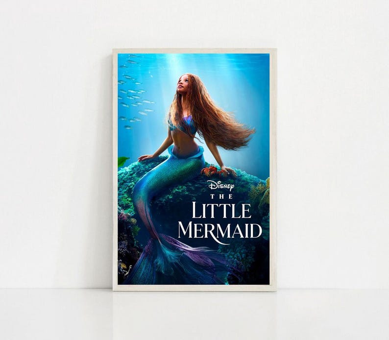 Puede incluir: Un p&oacute;ster enmarcado de "La Sirenita" de Disney. La imagen muestra a una sirena con largo cabello casta&ntilde;o rojizo y una cola turquesa, sentada en una roca. El fondo representa una escena submarina con luz solar y peces.