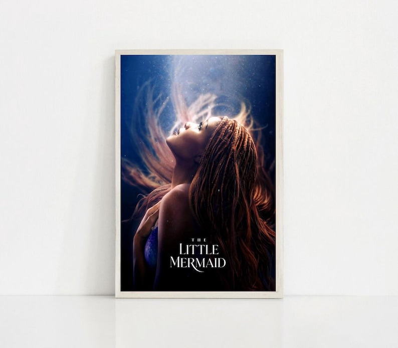 Puede incluir: Un p&oacute;ster enmarcado que presenta a una mujer con largo cabello casta&ntilde;o rojizo que fluye, mirando hacia arriba. La imagen tiene un tema submarino azul y blanco, con el texto "THE LITTLE MERMAID" en blanco en la parte inferior. El p&oacute;ster est&aacute; sobre un fondo blanco.