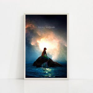 Puede incluir: Impresi&oacute;n enmarcada de una sirena sentada en una roca en el oc&eacute;ano. La sirena tiene pelo largo rojo y una cola verde y azul. El fondo muestra un cielo dram&aacute;tico con el texto "THE LITTLE MERMAID".