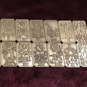 Op de afbeelding: Een set van 20 zilverkleurige metalen kaarten met zwart-wit illustraties van stokfiguren en symbolen. De kaarten zijn genummerd van I tot XX.