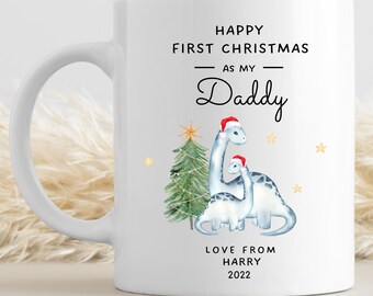 Può includere: Tazza in ceramica bianca con un design natalizio con due dinosauri blu che indossano cappelli di Babbo Natale. Il testo recita "Buon primo Natale come mio papà Amore da Harry 2022".