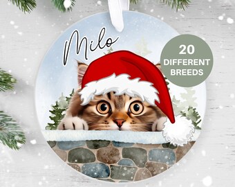 May include: A round Christmas ornament featuring a cat wearing a Santa hat peeking over a stone wall. The ornament is white with a blue background and the name "Milo" is written at the top. The text "20 DIFFERENT BREEDS" is written in a circle on the right side of the ornament.