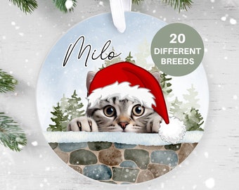 May include: A round Christmas ornament featuring a cat wearing a Santa hat peeking over a stone wall. The ornament is white with a blue and white winter scene. The cat's name, "Milo", is written in cursive at the top of the ornament. The text "20 Different Breeds" is written in green on a white circle in the upper right corner of the ornament.
