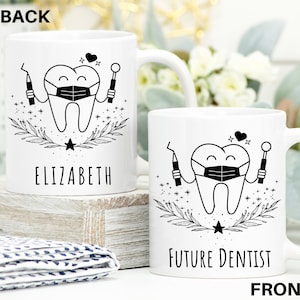 May include: White ceramic mug with a black and white illustration of a tooth wearing a face mask and holding dental tools. The text "FUTURE DENTIST" is printed on the front of the mug.