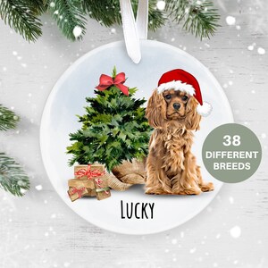 May include: A circular Christmas decoration with a Cavalier King Charles Spaniel wearing a Santa hat. A green Christmas tree with a red bow, wrapped gifts, and the word "LUCKY" are also depicted. The text "38 DIFFERENT BREEDS" is also included.