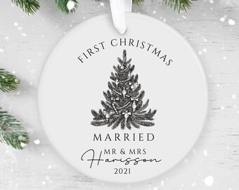 May include: White round Christmas ornament with a black and white illustration of a Christmas tree and the text "First Christmas Married Mr & Mrs Harrison 2021".