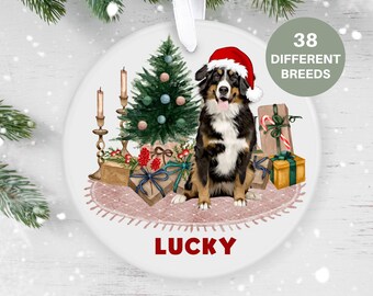 May include: A white ceramic Christmas ornament featuring a Bernese Mountain Dog wearing a Santa hat, sitting in front of a Christmas tree with presents and candles. The ornament is personalized with the name "LUCKY".