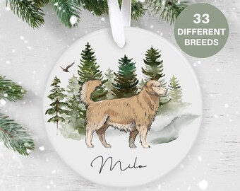 May include: A white ceramic ornament with a watercolor illustration of a golden retriever dog standing in a forest. The dog is brown and white and has a long tail. The forest is green and has a light blue sky in the background. The ornament has a white ribbon attached to the top and the name "Milo" written in black cursive at the bottom.