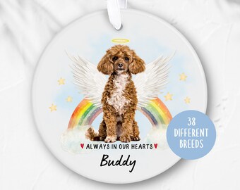 May include: A circular ceramic ornament with a brown poodle depicted with angel wings and a halo, set against a rainbow. Text reads "ALWAYS IN OUR HEARTS" and "Buddy". A blue circle says "38 DIFFERENT BREEDS". Includes a white ribbon for hanging.