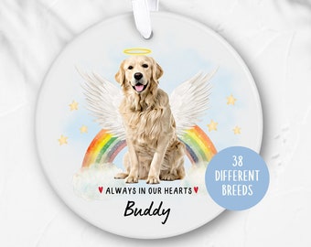 Könnte beinhalten: Weißer Keramik-Anhänger mit einem Regenbogen, Wolken und einem Golden Retriever mit Engelsflügeln. Der Text "Immer in unseren Herzen" und der Name "Buddy" stehen unter dem Hund. Der Text "38 verschiedene Rassen" befindet sich in einem blauen Kreis auf der rechten Seite des Anhängers.