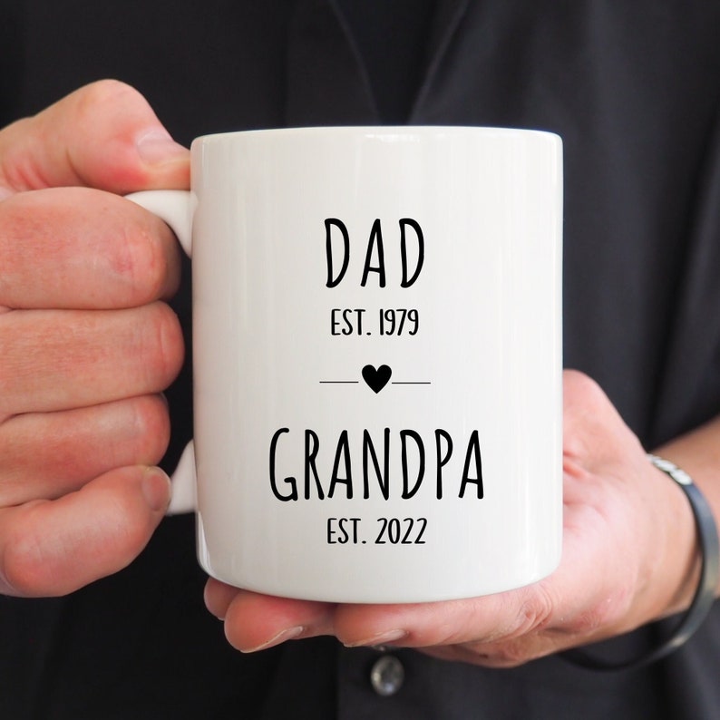 May include: White ceramic mug with black text that reads "Dad Est. 1979" with a small black heart and a line below it. The text below the line reads "Grandpa Est. 2022".