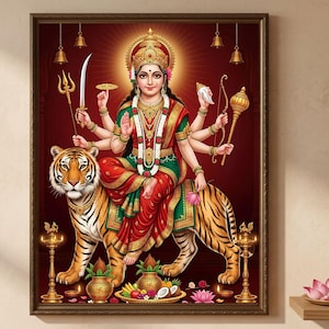 May include: A framed wall art print depicting the Hindu goddess Durga with eight arms, wearing a red and green sari and gold jewelry, seated on a tiger. She holds various symbolic items including a sword, trident, conch, and mace. Brass lamps and offerings are at the base.