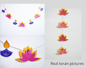 May include: Paper garlands featuring lotus flower and oil lamp designs in pink, yellow, and blue. The garlands are strung on white string and are displayed against a white background. Text on the image reads "Twinkles on the way" and "Real toran pictures."