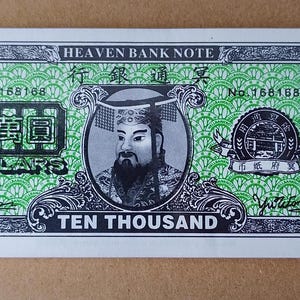 May include: A rectangular Heaven Bank Note featuring a green patterned background with black ink details. The note displays the text HEAVEN BANK NOTE, TEN THOUSAND, and DOLLARS, along with a central portrait of a figure in traditional headwear.
