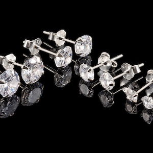 May include: A set of eight silver stud earrings with clear cubic zirconia stones. The earrings are arranged in a row on a black background.