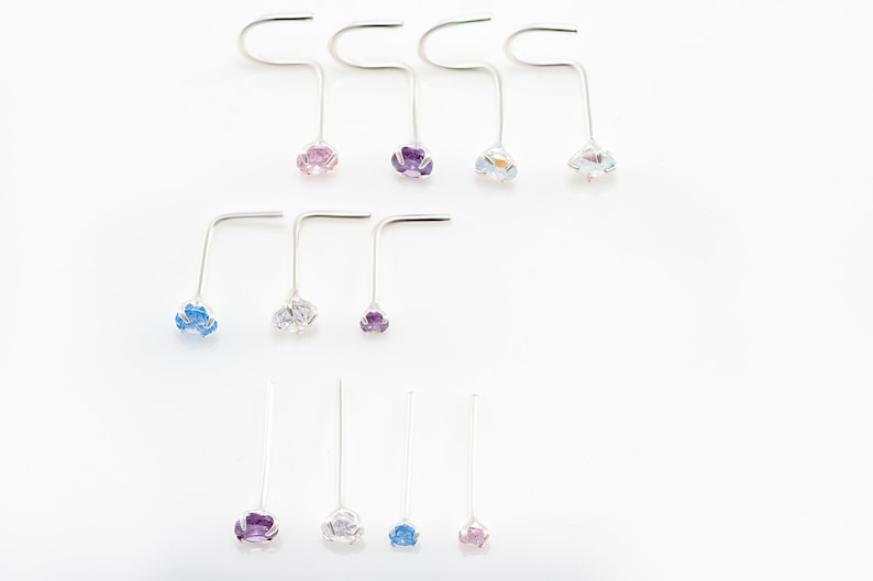 May include: A set of ten nose rings with different colored gemstones. The rings are made of silver and have a simple, elegant design. The gemstones are pink, purple, blue, and clear.