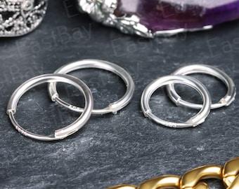 May include: Four silver hoop earrings with a hinged clasp. The earrings are arranged in a row on a dark gray surface.