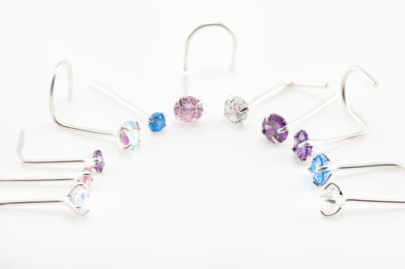 May include: A set of eight nose rings with different colored gemstones. The rings are made of silver and have a simple, elegant design.