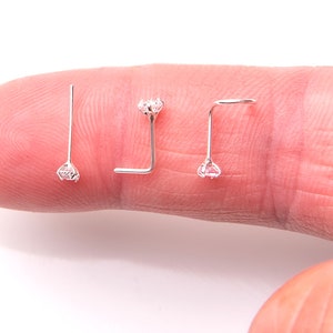 May include: Three silver nose rings with clear rhinestones. The rings are on a finger.