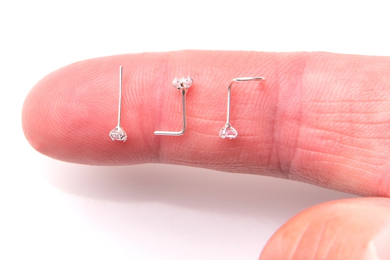 May include: Three silver nose rings with clear rhinestones. The rings are on a finger.