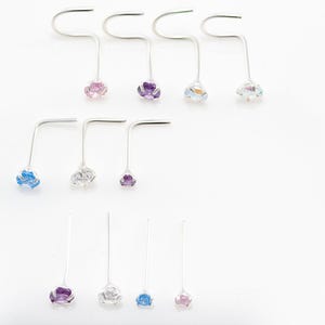May include: Assortment of nose rings with different colored gemstones. The rings are made of silver and have a curved shape. The gemstones are blue, purple, and pink.