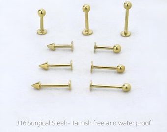 May include: Gold-coloured body jewellery, including barbell and arrow-shaped studs. The image text reads "316 Surgical Steel: - Tarnish free and water proof." Sizes include 1.0mm, 1.2mm, 1.6mm, 6mm, 8mm, and 10mm.