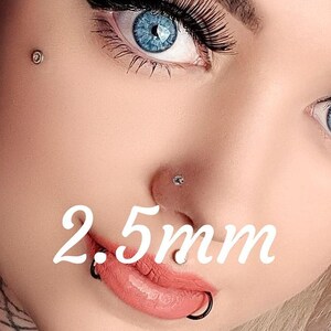 May include: Close-up of three different sizes of nose rings, 2mm, 2.5mm, and 3mm. The rings are made of silver and are worn by a person with blonde hair and blue eyes.