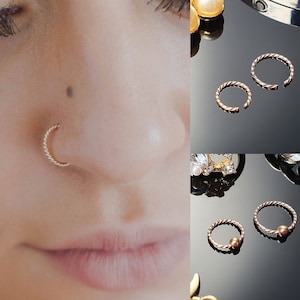 Puede incluir: Dos juegos de aros para la nariz de oro. Un juego es liso y el otro tiene una pequeña perla en el aro. Los aros están hechos de alambre trenzado.