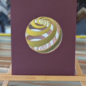 May include: A maroon mat with a circular cutout revealing a yellow, green, and pink spiral pattern.