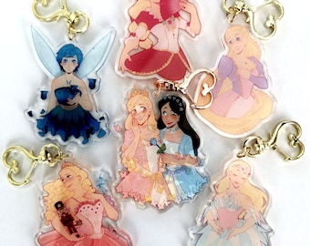 May include: Set of seven colorful character charm keychains featuring a fairy, a ballerina, and five princesses. The charms are made of clear acrylic and have gold heart-shaped key rings.
