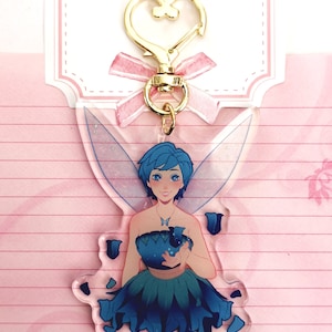 May include: A blue fairy with wings and a blue flower dress holding a blue flower. The fairy is a keychain with a gold heart-shaped clasp.