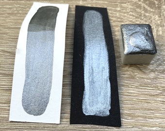 May include: Two swatches of silver metallic paint, one on white paper and one on black paper, and a small silver metallic paint pan.