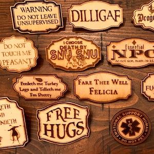 May include: A collection of wooden signs with various engraved phrases and sayings. The signs are in different shapes and sizes, with text like "Warning Do Not Leave Unsupervised" and "Free Hugs". The signs are arranged on a wooden surface.