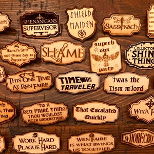 May include: A collection of laser-cut wooden signs with various humorous phrases and quotes. The signs are in different shapes and sizes, with dark brown text on a light brown background. The signs are arranged on a wooden surface.