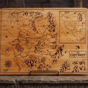 May include: A rectangular bamboo cutting board with a detailed map of a fantasy continent etched into its surface. The map includes geographical features, place names, and a compass rose. The text "THE CONTINENT" is at the bottom.
