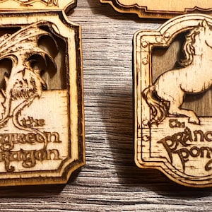 May include: Two wooden signs with engraved images and text. The first sign features a green dragon with the text "The Green Dragon". The second sign features a white horse with the text "The Prancing Pony".