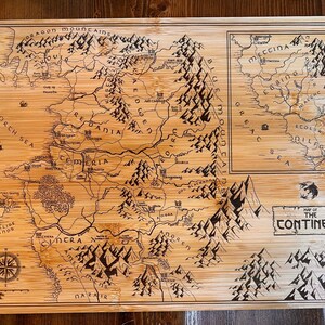 May include: A wooden cutting board with a map of a fictional continent engraved on it. The map is in black and white and features mountains, rivers, and cities. The text "Map of the Continent" is engraved at the bottom of the board.
