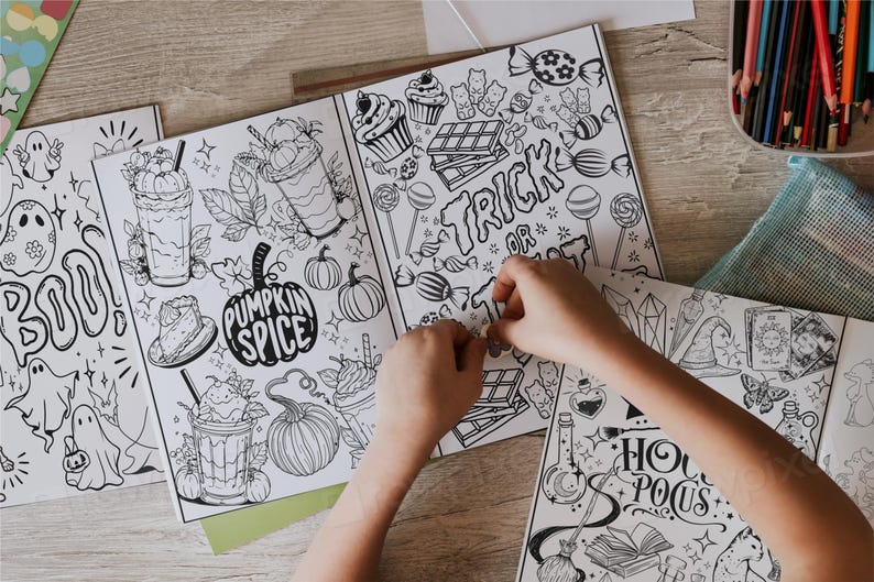 May include: A set of five coloring books with Halloween and fall themes. The books feature illustrations of ghosts, pumpkins, candy, and other spooky and festive imagery. The books are open and a child's hands are coloring one of the pages.